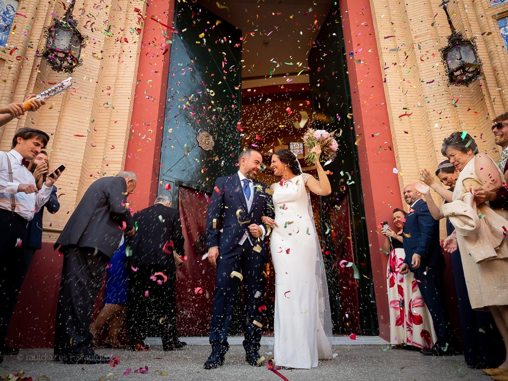 Pareja recién casada saliendo de la iglesia entre confeti, fotografiada por Raúl Díaz