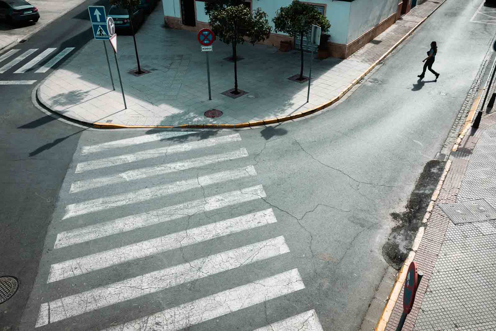 Persona cruzando una calle de Dos Hermanas junto a un gran paso de peatones y sombras nítidas.