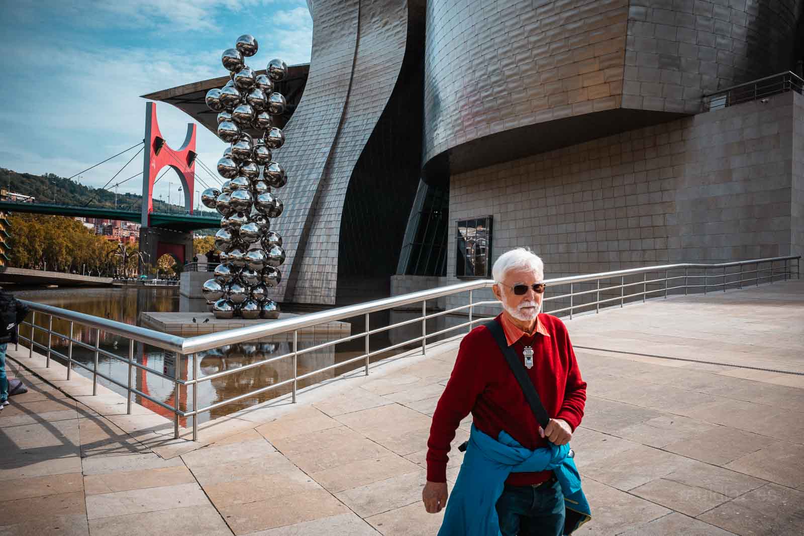 Visitante vestido de rojo ante el Guggenheim, la escultura de esferas y el puente de La Salve