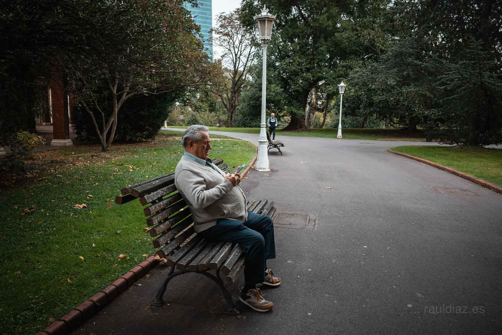 Hombre sentado en un banco de un parque de Bilbao mirando el móvil