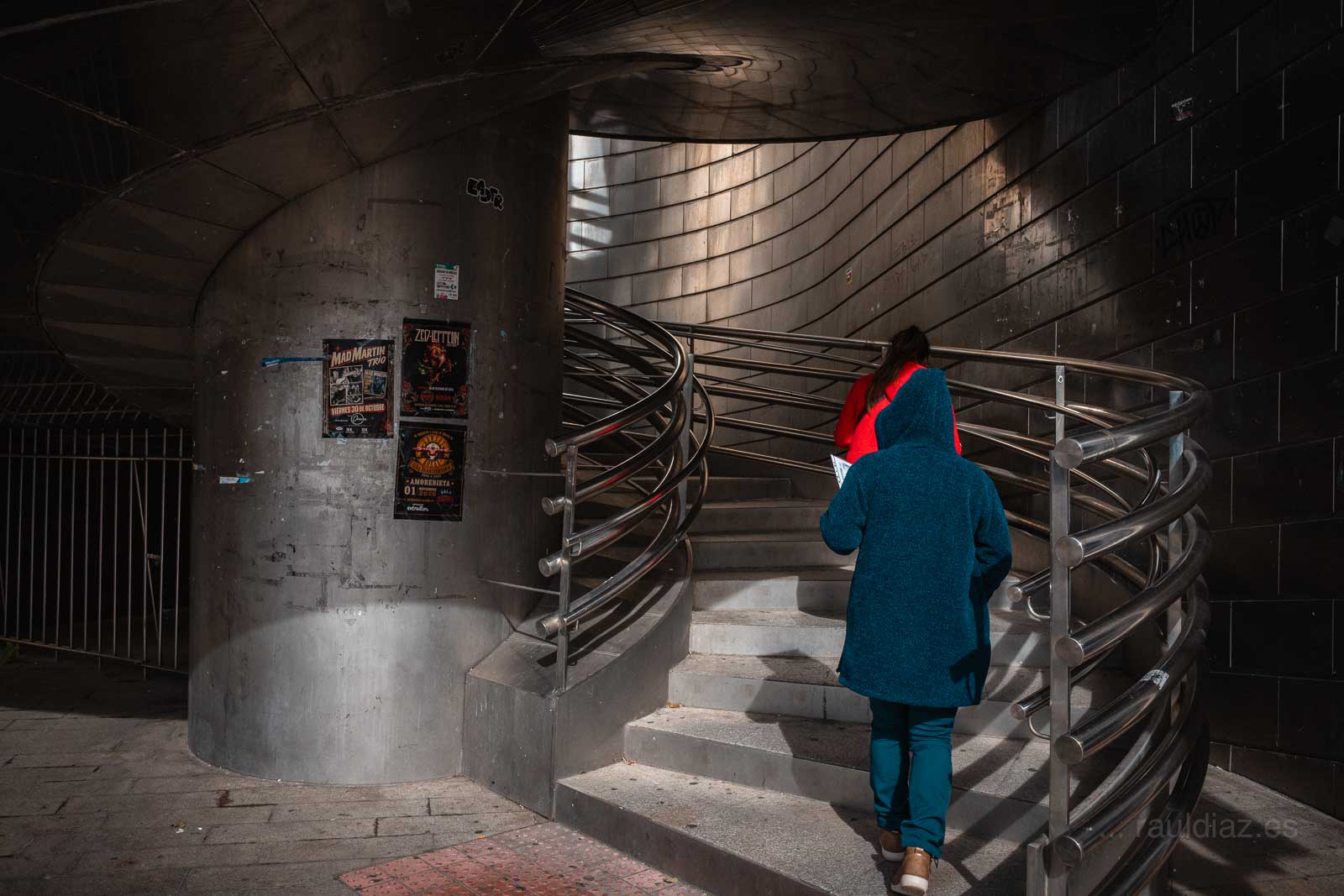 Dos mujeres subiendo por la escalera circular, una de rojo y otra de azul